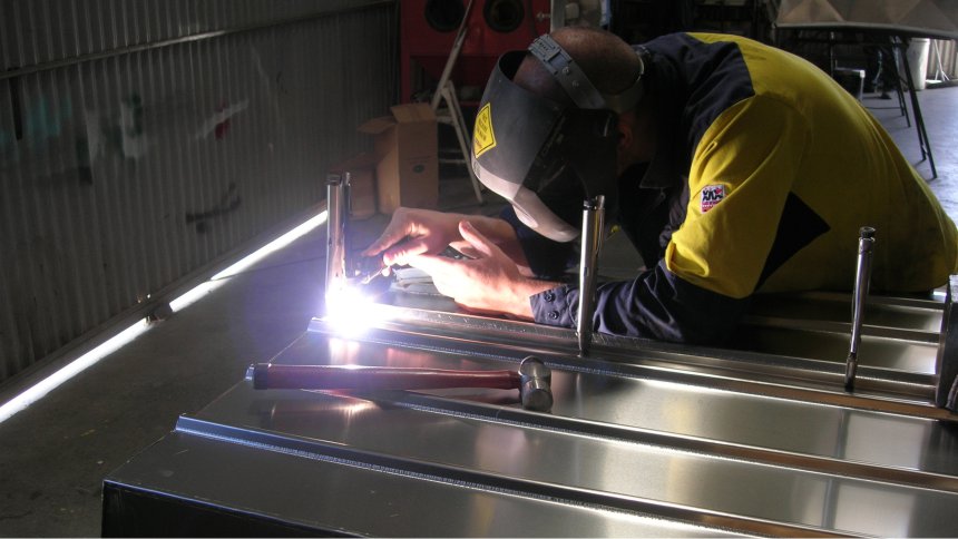 A man welds a custom aluminum boat in an Australian manufacturing facility